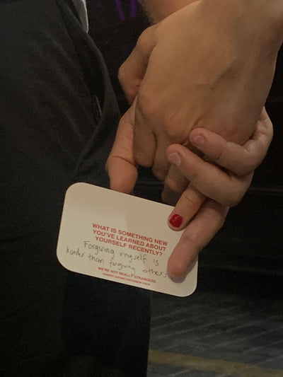 We're Not Really Strangers Honest Dating Expansion Pack. Two people holding hands and card reading "What is something new you've learned about yourself recently?" with handwriting reading "Forgiving myself is harder than forgiving others."