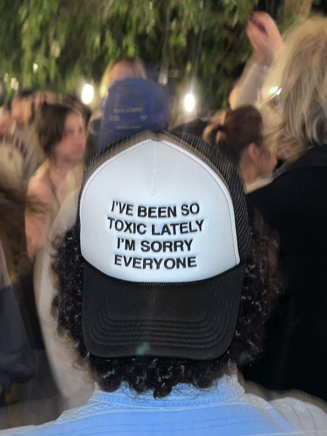 Person wearing We're Not Really Strangers Black I've Been So Toxic Lately Trucker Hat reading "I've Been So Toxic Lately I'm Sorry Everyone" in black embroidery on the front white panel of hat.