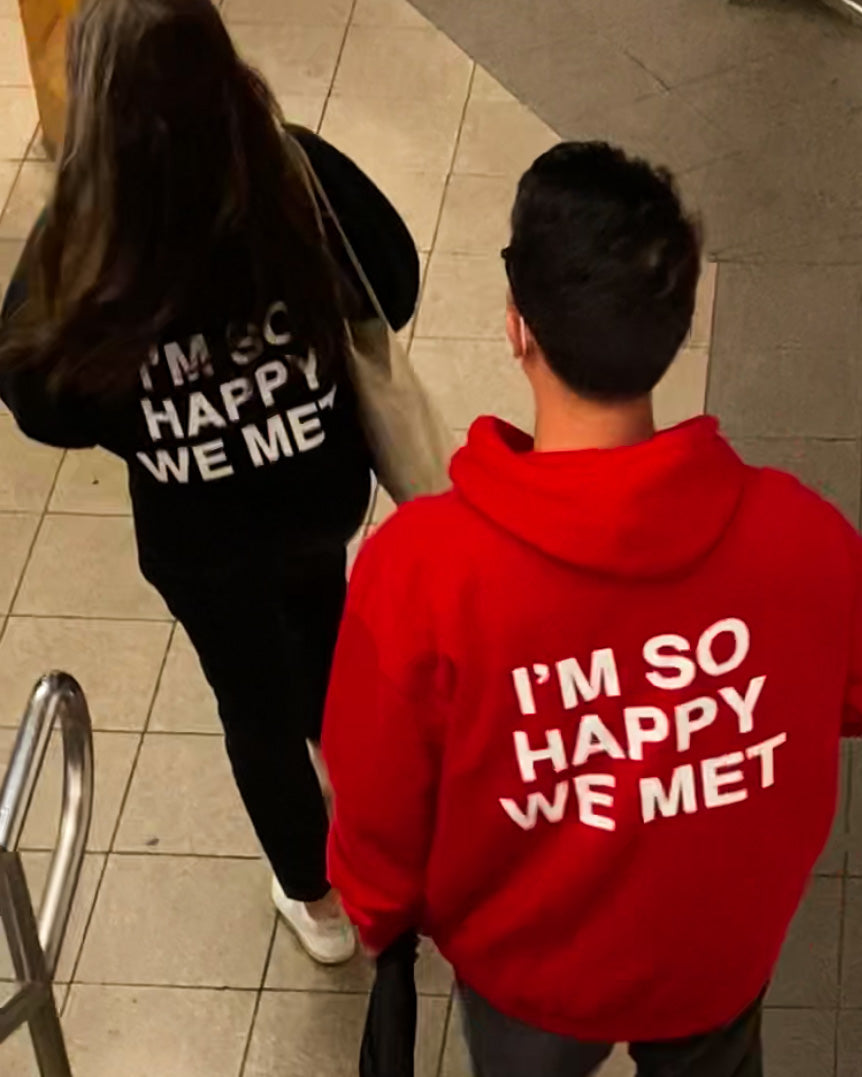 Black hoodie with white text reading "I'm So Happy We Met" on the back, shown from above on a person.