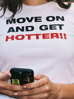 White baby tee with black and red text reading "Move On And Get Hotter!!" worn with a phone in hand.
