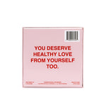 Pink board game box with red text reading "You deserve healthy love from yourself too" and barcode label.