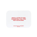 White card with red text reading "Write a letter to your younger self. Tell them how you're doing" and "We're not really stra
