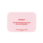 Pink rounded rectangle card with red text reading "REMINDER NOT EVERY STEP YOU TAKE WILL BE FORWARD" and "WE'RE NOT REALLY ST
