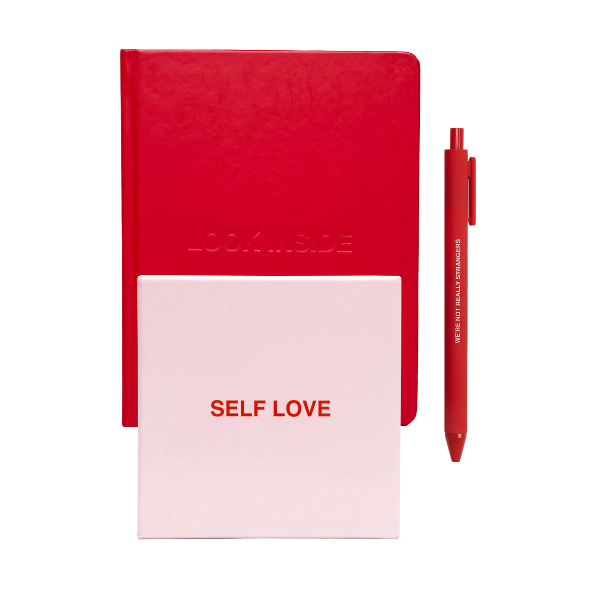 Red notebook with embossed text, pink notepad with "Self Love" text, and red pen with white text.