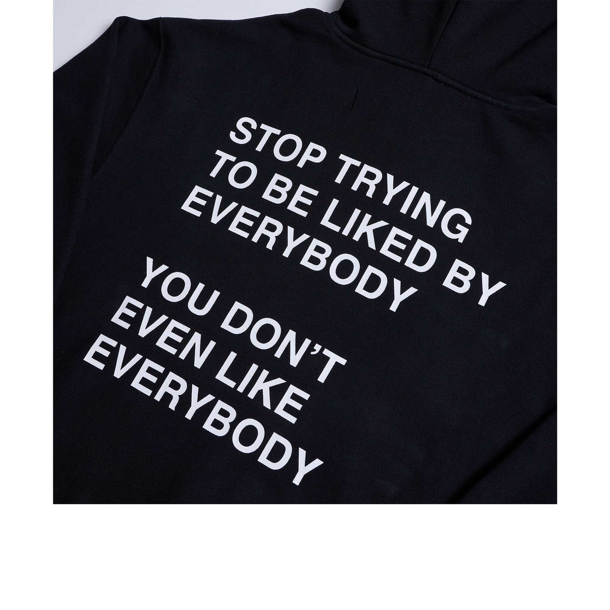 Black hoodie with white text reading "Stop Trying To Be Liked By Everybody You Don't Even Like Everybody"