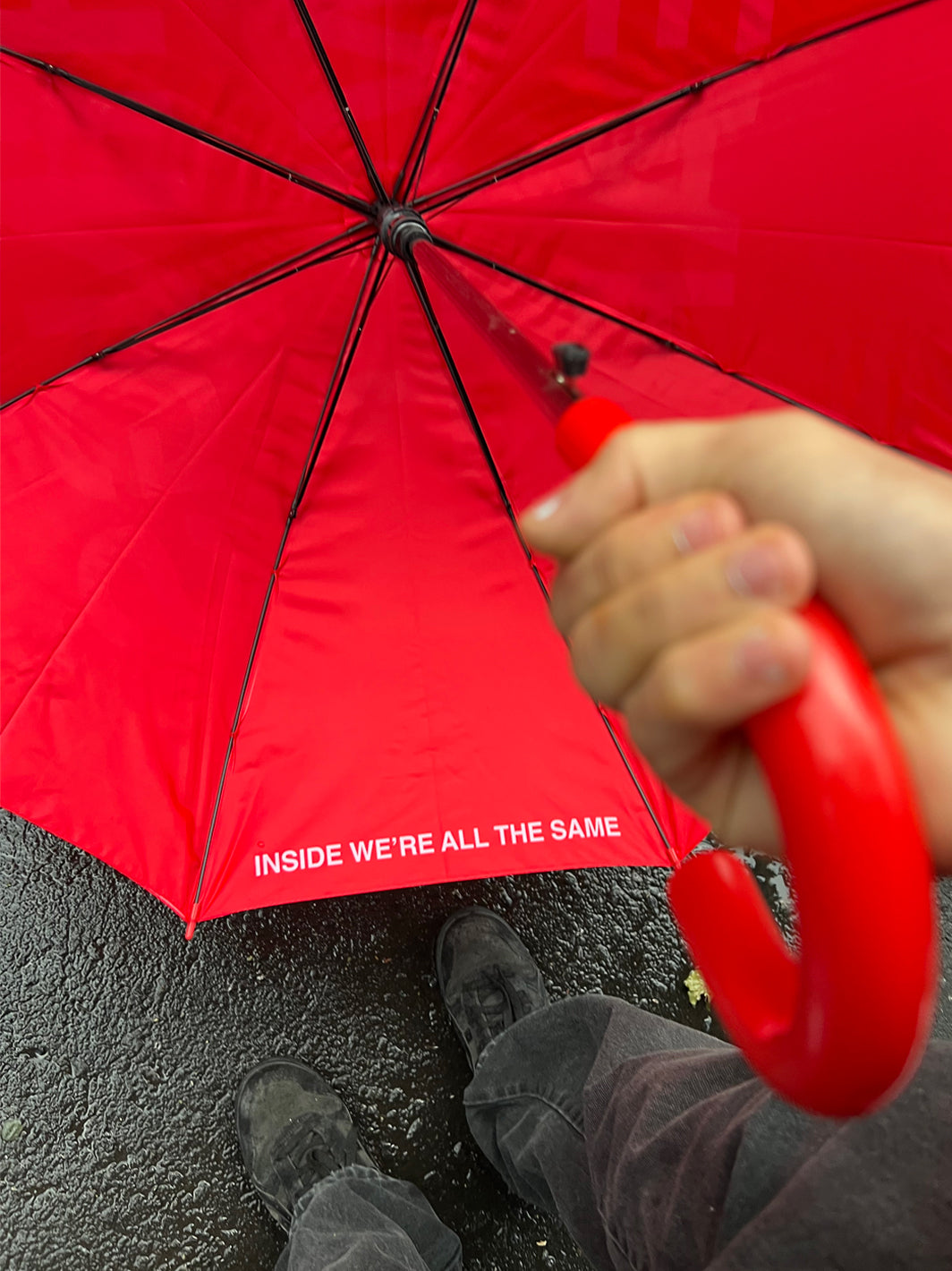 Red umbrella with black spokes held overhead, showing interior text and person's hand and feet below.
