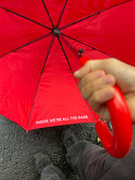 Red umbrella with black spokes held overhead, showing interior text and person's hand and feet below.