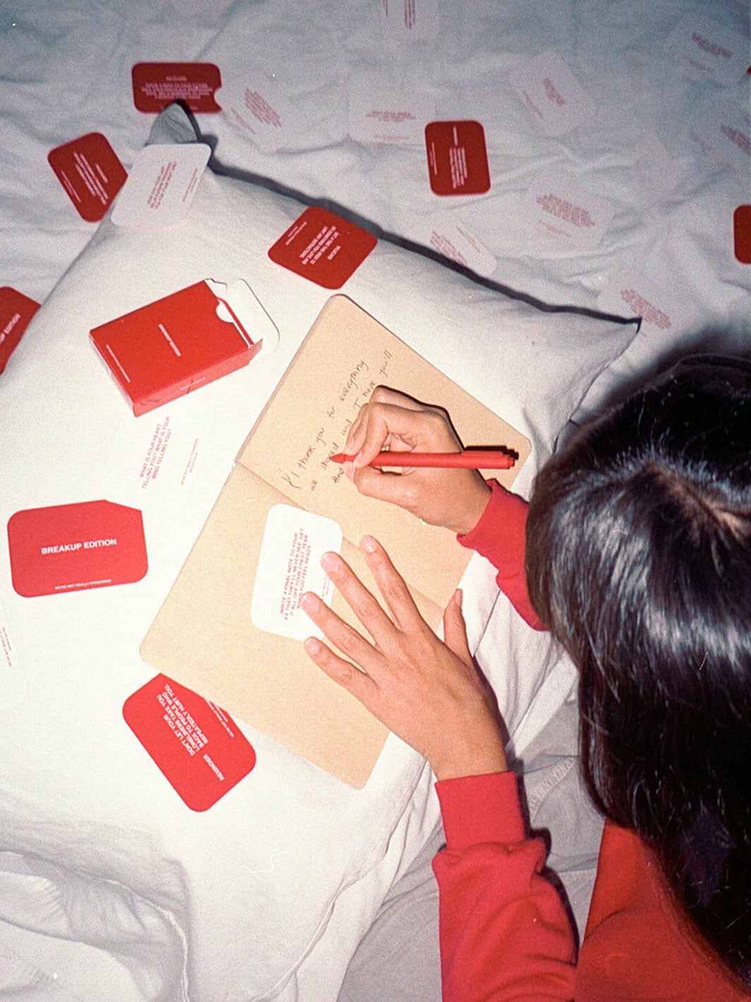 Person writing on beige paper with red marker surrounded by red cards and envelopes on white fabric.