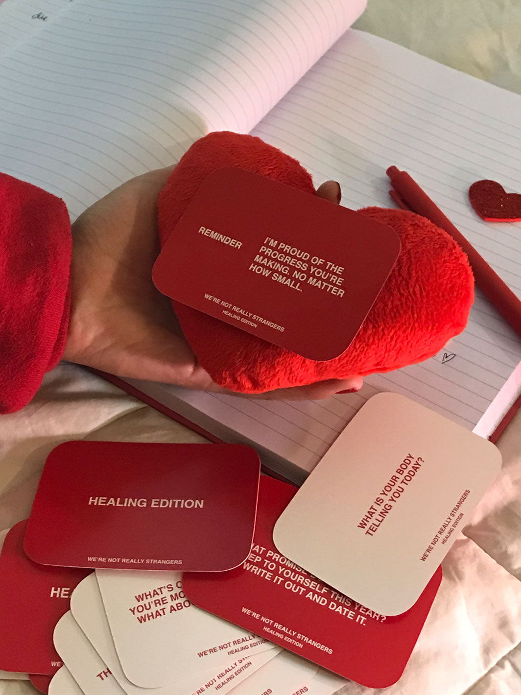 Red plush heart-shaped pillow with affirmation cards displayed on open notebook pages.