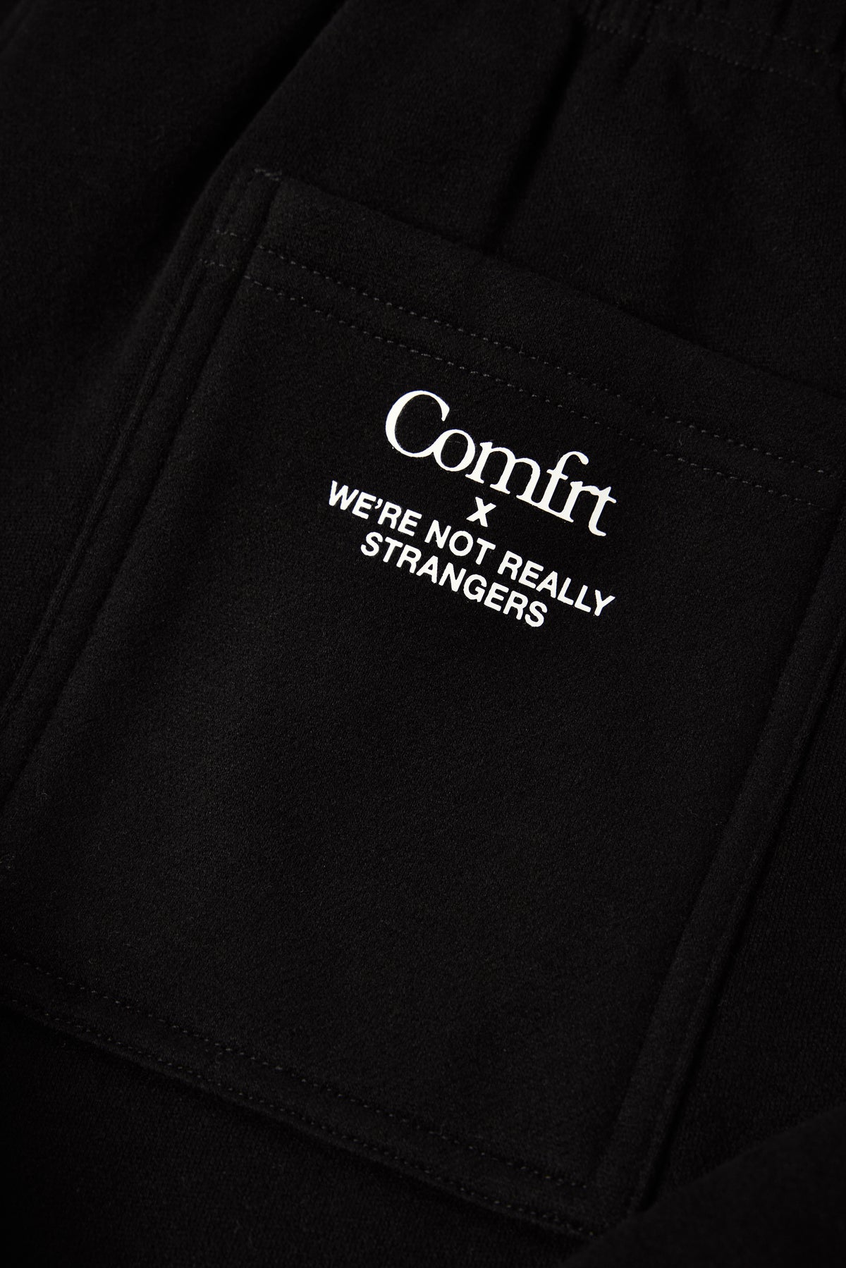 Black sweatshirt with white text reading "Comfrt x WE'RE NOT REALLY STRANGERS" printed on front pocket.