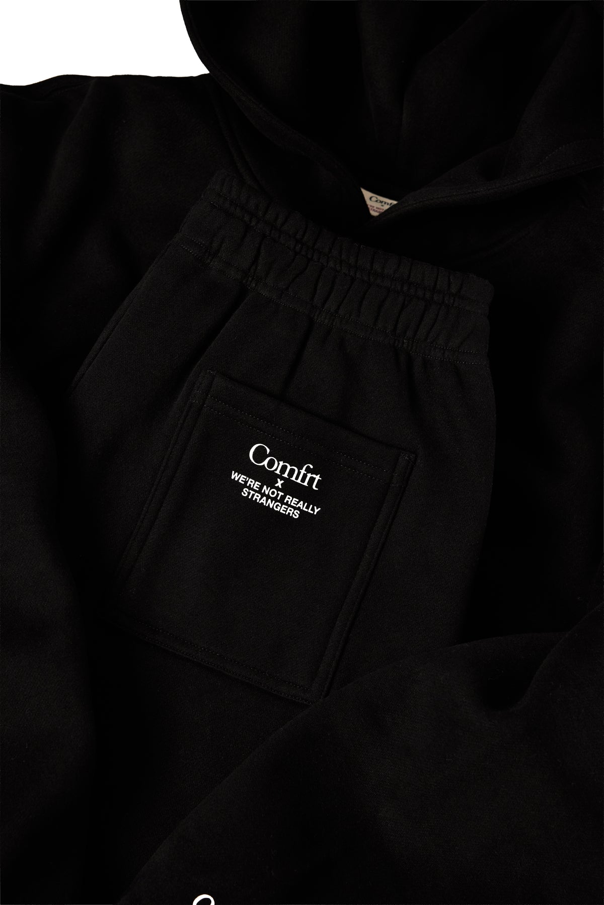 Black sweatshirt and sweatpants set with small triangular logo on chest and text graphic on pants pocket.