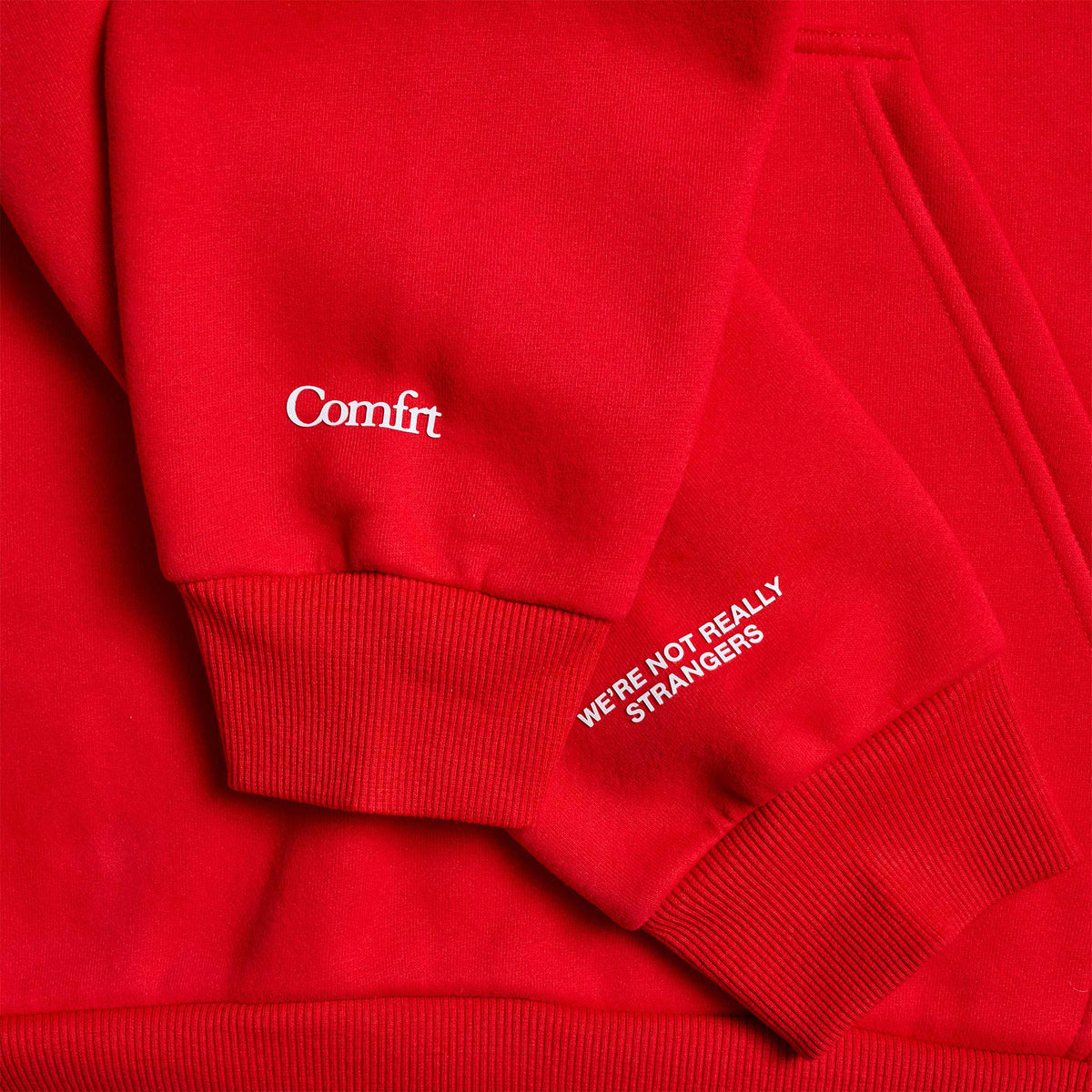Red hoodie with "Comfrt" text on chest and "We're not really strangers" text on sleeve, ribbed cuffs and hem visible.