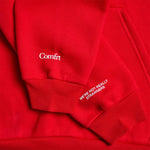 Red hoodie with "Comfrt" text on chest and "We're not really strangers" text on sleeve, ribbed cuffs and hem visible.