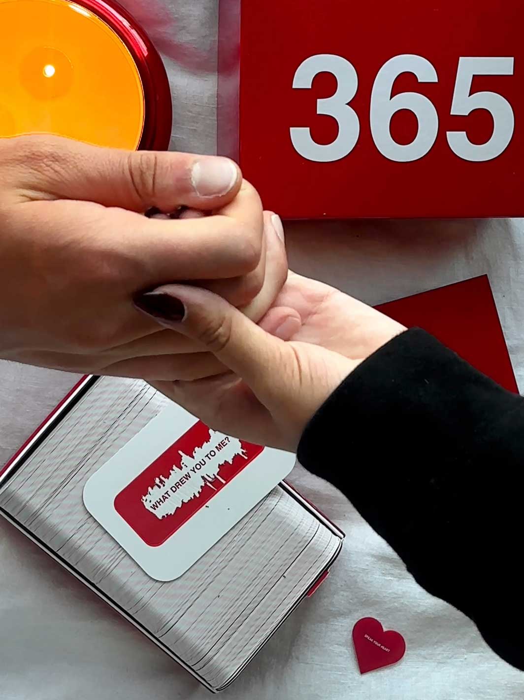 Two hands holding an open book with red and white pages, yellow circular object above, and "365" displayed on red background.