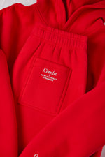 Red sweatpants with elastic waistband and patch pocket featuring white text branding.