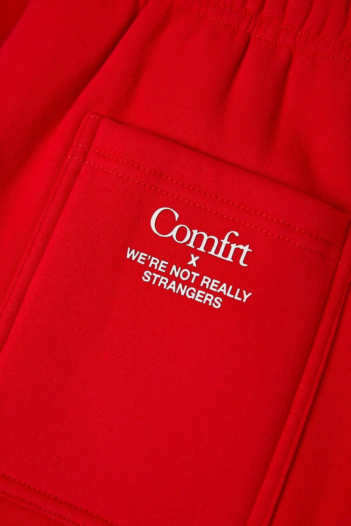Red sweatpants with white embroidered "Comfrt x We're Not Really Strangers" text and stitched seams.