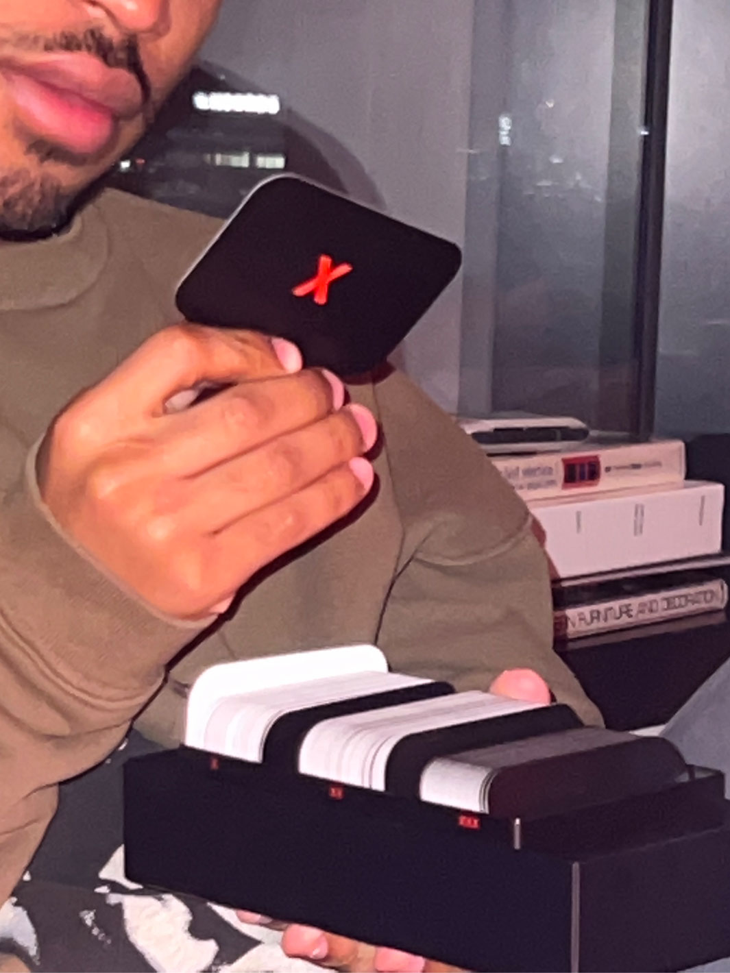 Hand holding small black streaming device with red X logo next to white and black remote controls.