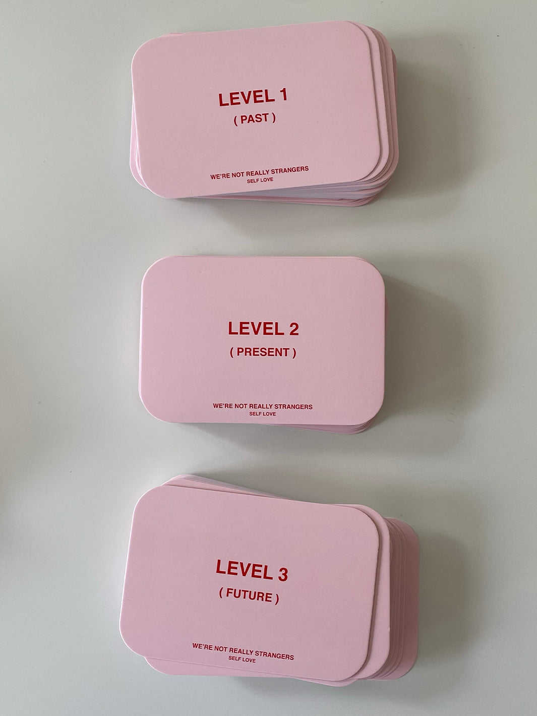 Three pink card decks labeled Level 1 (Past), Level 2 (Present), and Level 3 (Future) with "We're Not Really Strangers Self L