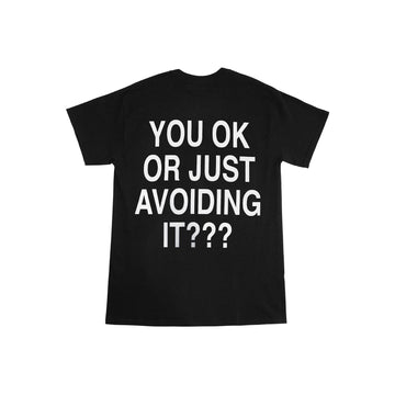 We're Not Really Strangers Mental Health Awareness Month. Back view of black You Ok Or Just Avoiding It Tee with large white font reading 