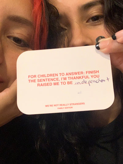 We're Not Really Strangers two people holding up Family Edition card reading "For children to answer: finish the sentence, I'm thankful you raised me to be___" with handwriting  on card reading "independent."