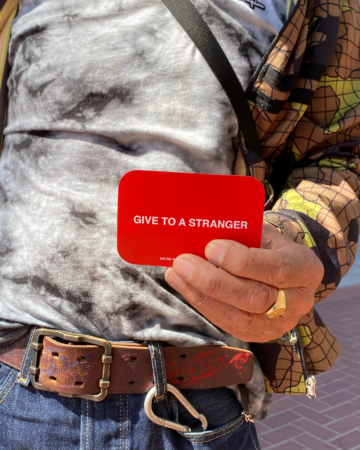 We're Not Really Strangers Give to a Stranger Pack. Person outdoors holding a red card reading "Give to a Stranger" in white font. Back view of Give to a Stranger card.