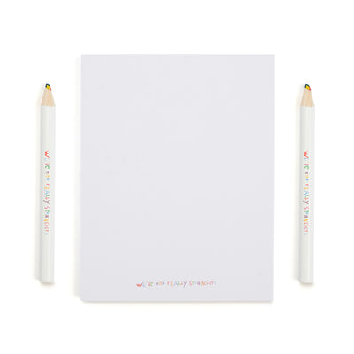 We're Not Really Strangers Kids Edition. Front facing view of Kids Edition white notepad and 2 rainbow colored pencils.